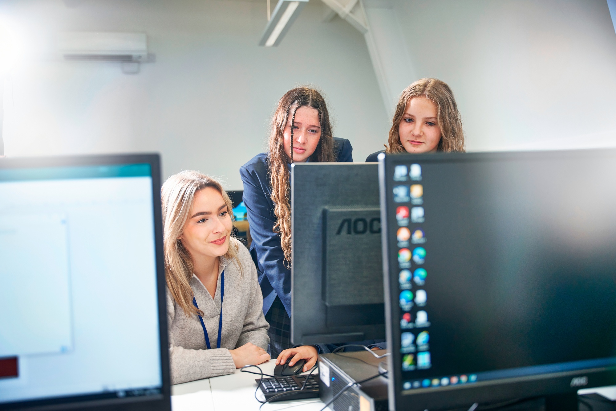 two female students with a female teacher looking at a computer science