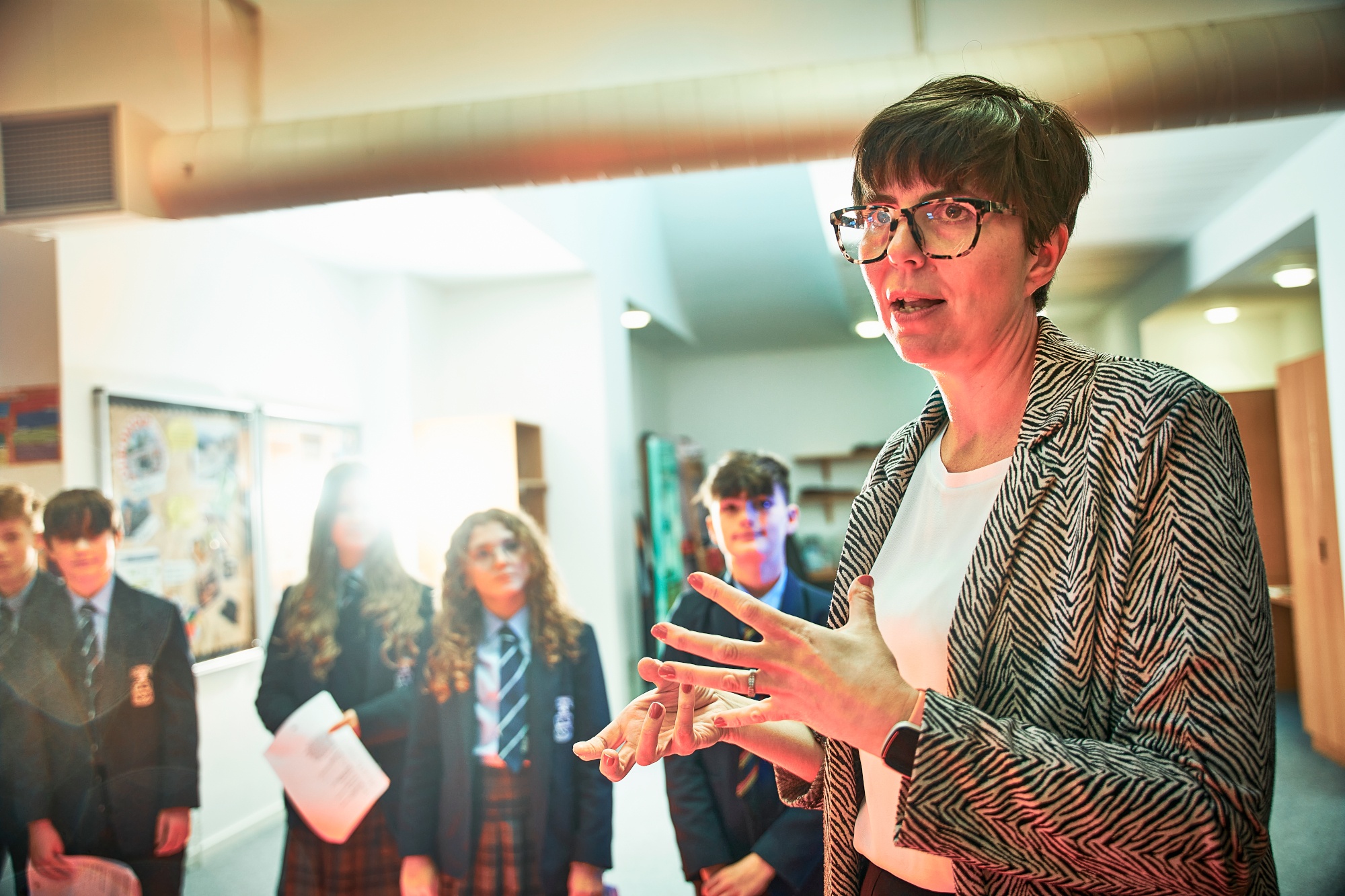 teacher standing in the foreground speaking animatedly to students in a drama class, with students in the background