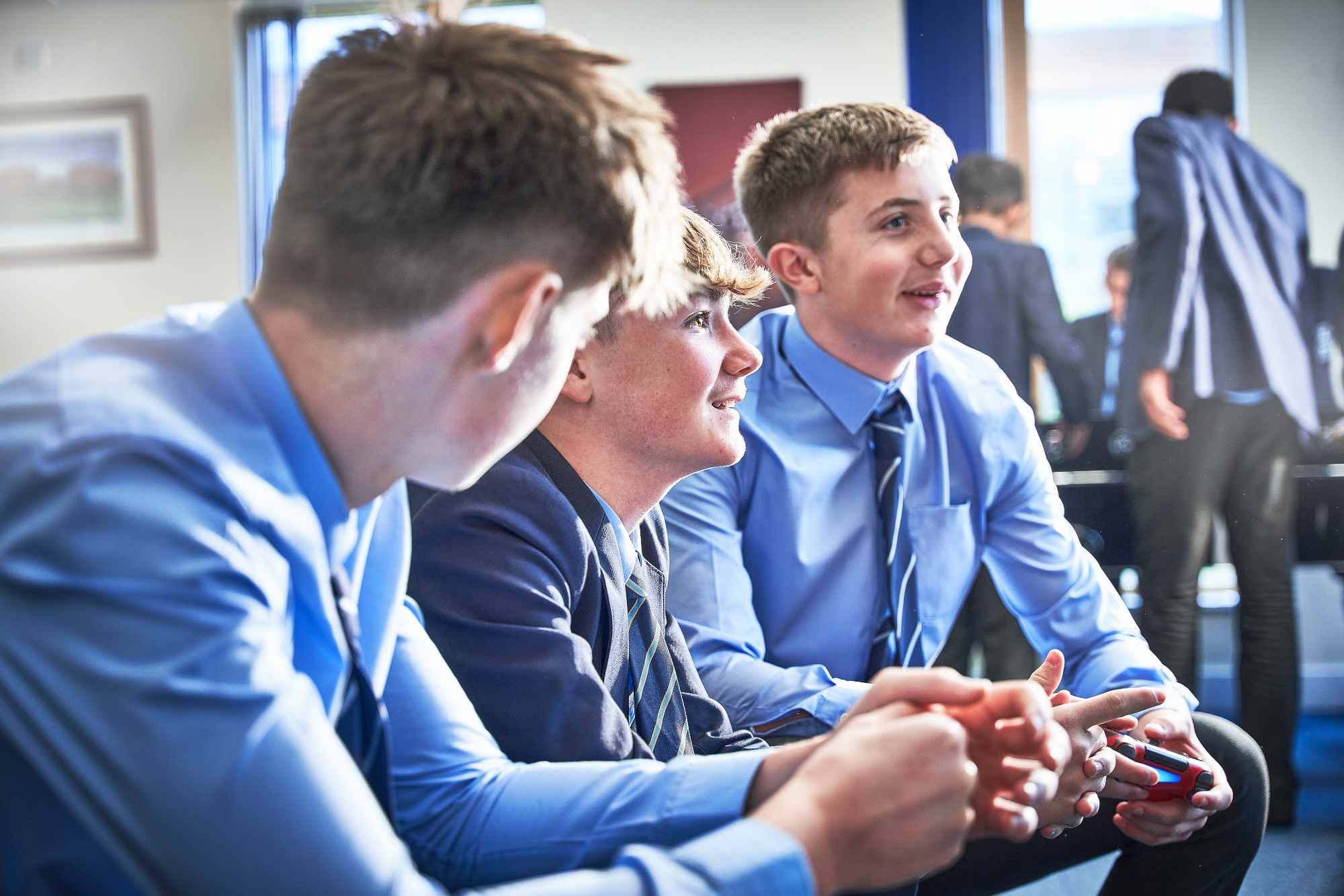 three boys sitting on sofas facing ahead gaming and talking