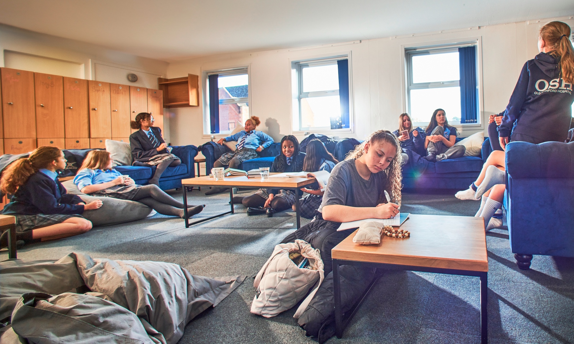 girl's boarding house large recreation room with girls of various ages sitting on sofas chatting and studying