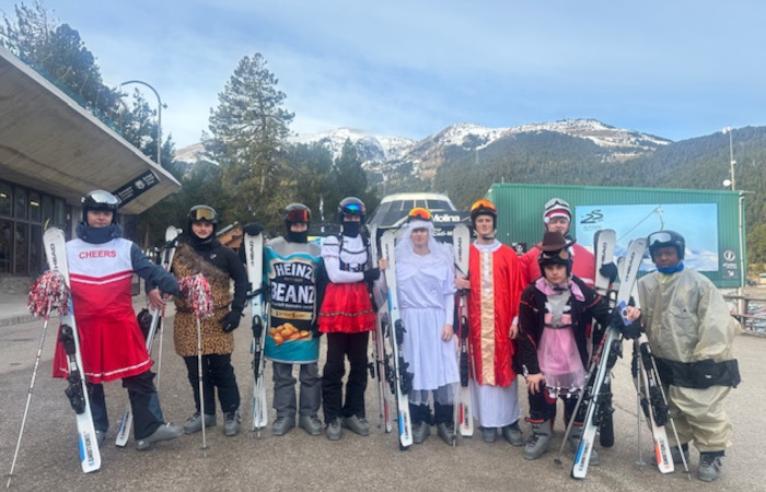 A group of Year 11 boys stand in various fancy dress costumes including Father Christmas, a cheerleader and a tin of beans at the foot of a snowy mountain