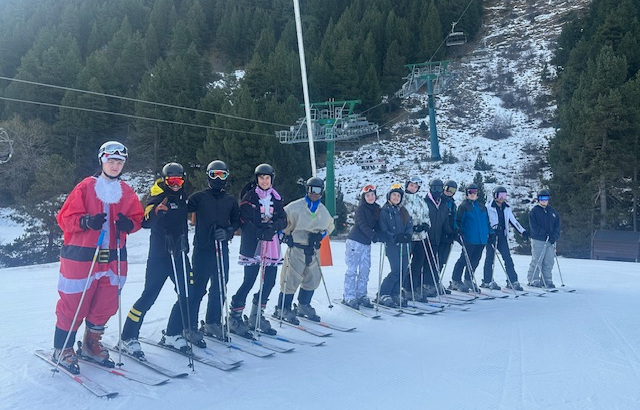 A large group of students stand on skis in the snow at the bottom of a ski lift