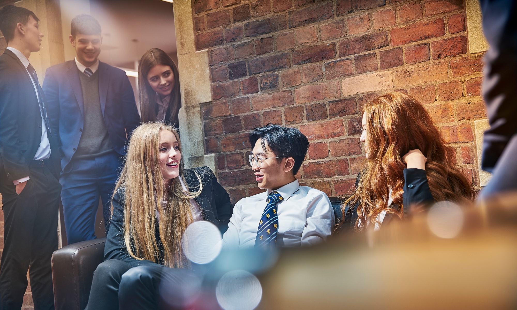 Selection of male and female students chatting on sofas in a common room, wearing suits