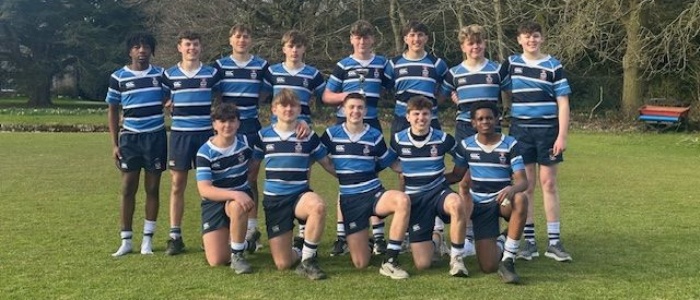 13 members of the Under 15 boys' rugby sevens team pose in kit with their winning trophy on a rugby pitch
