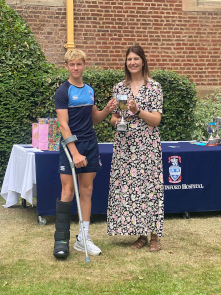 Male student wearing OSH sports kit and on crutches collects an award from Cat Eccles MP, shaking hands and smiling at the camera