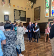 Two students in suits and prefect gowns being photographed by their parents infront of a stained glass window