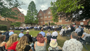Rows of students, families and friends seated in summer dress on the lawn of the rose garden with Founders' Building in the background