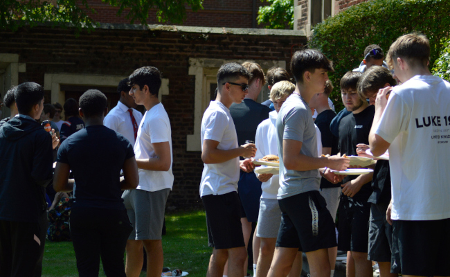 Groups of boys standing talking in their friendships groups enjoying a BBQ