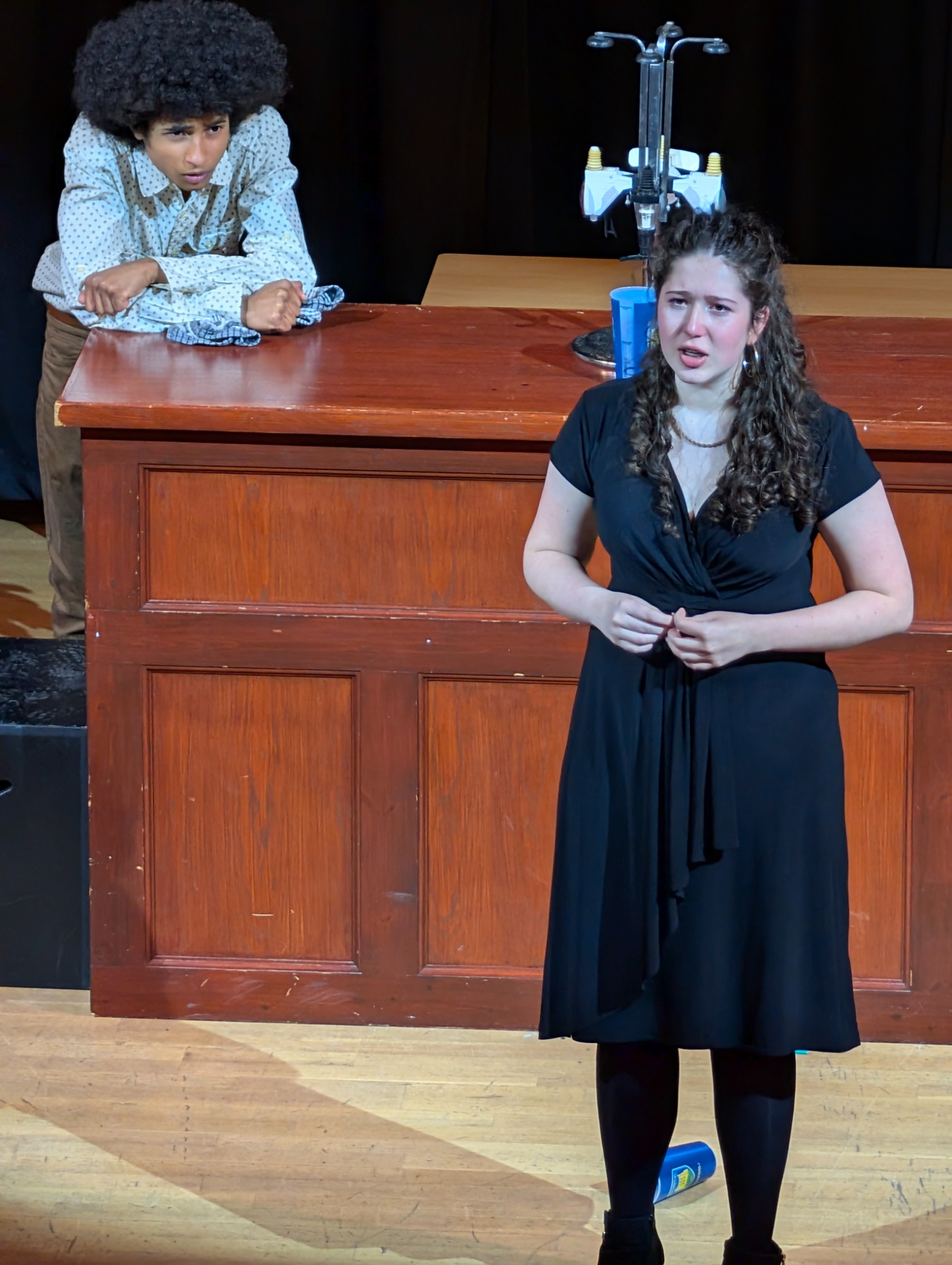 Two actors on stage looking thoughtful leaning on a bench